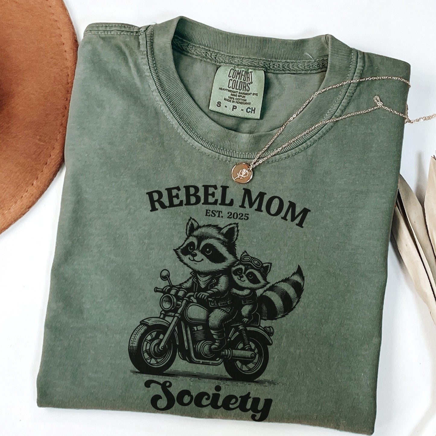 Somebody’s Rebel Wife mom life shirt designed with a playful raccoon motorcycle graphic, combining humor and fashion for moms who love standout style