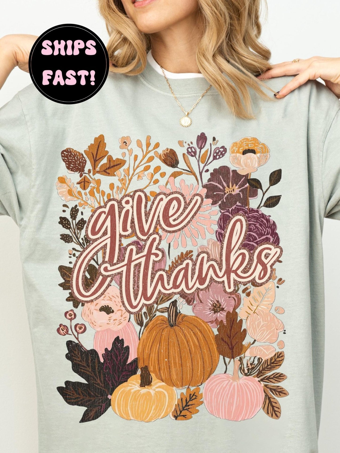 A woman wearing a light green t-shirt with a graphic design featuring autumn flowers, pumpkins, and the text &quot;Give Thanks&quot;