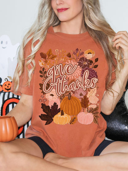 A woman wearing a t-shirt with a floral design and the text &quot;Give Thanks&quot; is sitting on a couch.