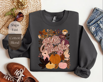 a gray sweatshirt with a floral design and the text &quot;Give Thanks&quot; printed on it, along with a pair of jeans and a pair of brown shoes.