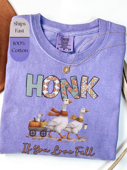The image is a purple t-shirt with a graphic design depicting a goose pulling a wagon with pumpkins, accompanied by the text &quot;HONK If You Love Fall&quot;.