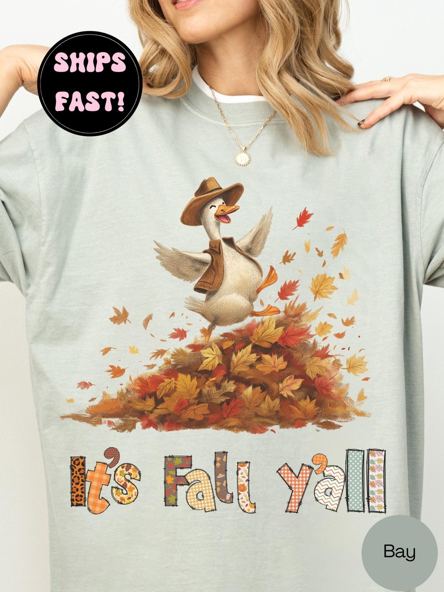 A person wearing a gray t-shirt with a graphic design depicting a cartoon goose surrounded by autumn leaves. The text on the t-shirt says &quot;It&#39;s Fall y&#39;all&quot; and there is a &quot;SHIPS FAST!&quot; sign above the image.