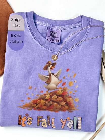 A purple t-shirt with a cartoon goose wearing a cowboy hat and surrounded by autumn leaves, with the text &quot;It&#39;s Fall y&#39;all&quot; printed on it.