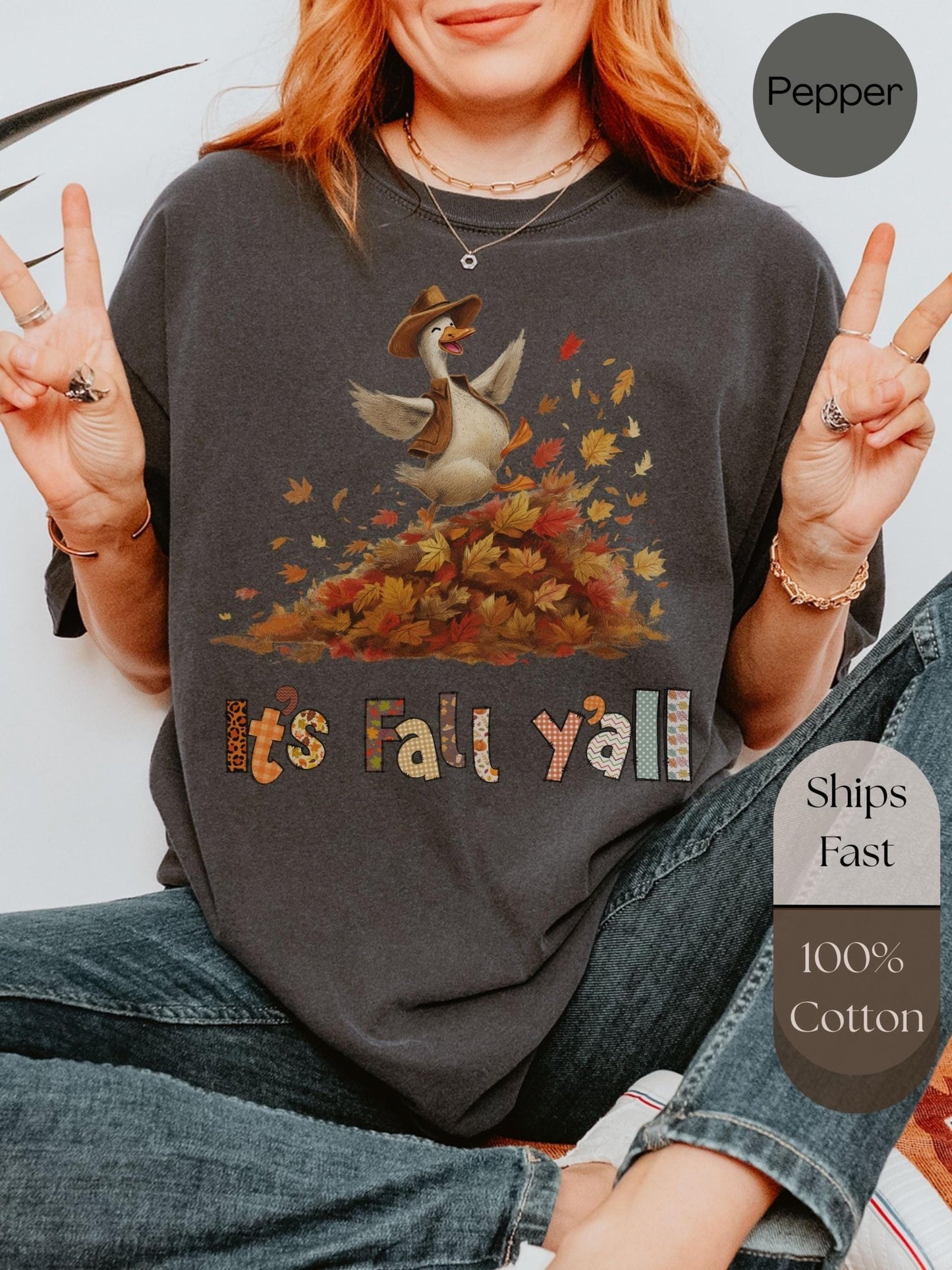 A person wearing a gray t-shirt with a graphic of a duck surrounded by autumn leaves and the text &quot;It&#39;s Fall y&#39;all&quot; is making a peace sign.