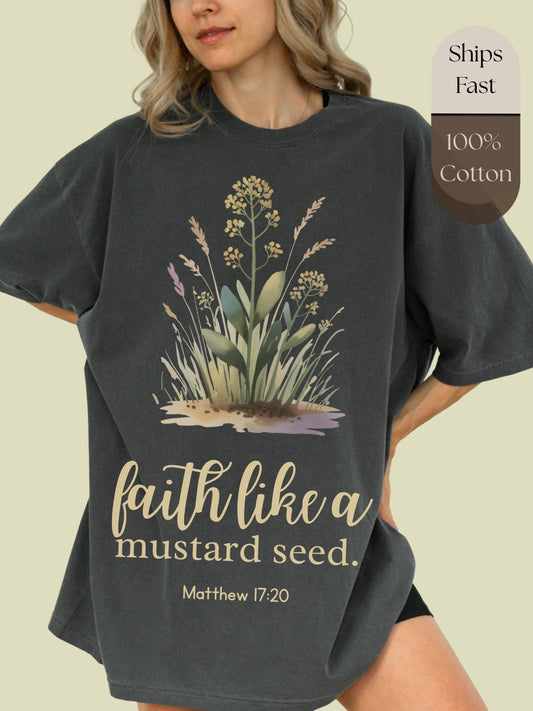 A woman wearing a gray t-shirt with a graphic design of a mustard seed and the text "faith like a mustard seed" printed on it.